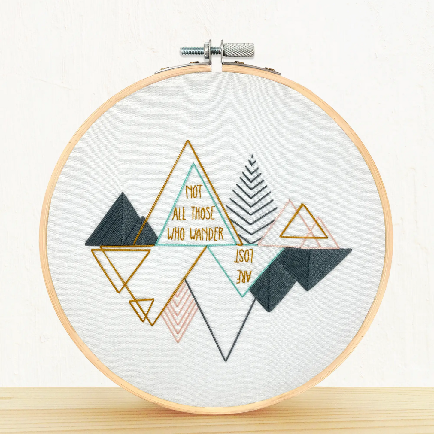 An embroidery hoop featuring a finished Wanderlust work . The needlepoint slogan reads;"Not all those who wander are lost".