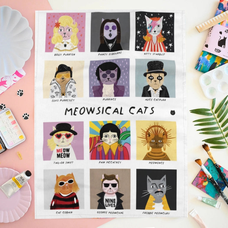 A tea towel featuring 'Meowsical Cats' with colorful cat illustrations on a pink background.