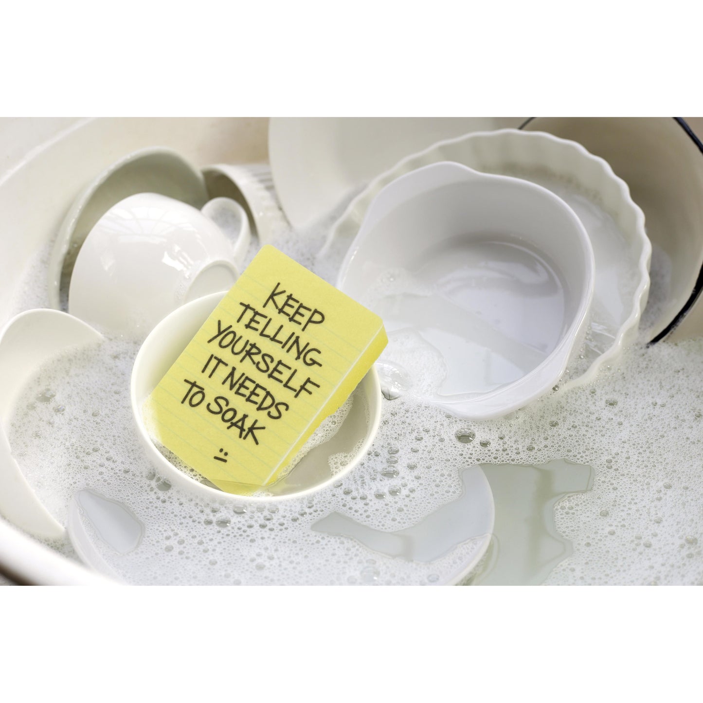a yellow sponge with text in a soapy kitchen sink with dishes