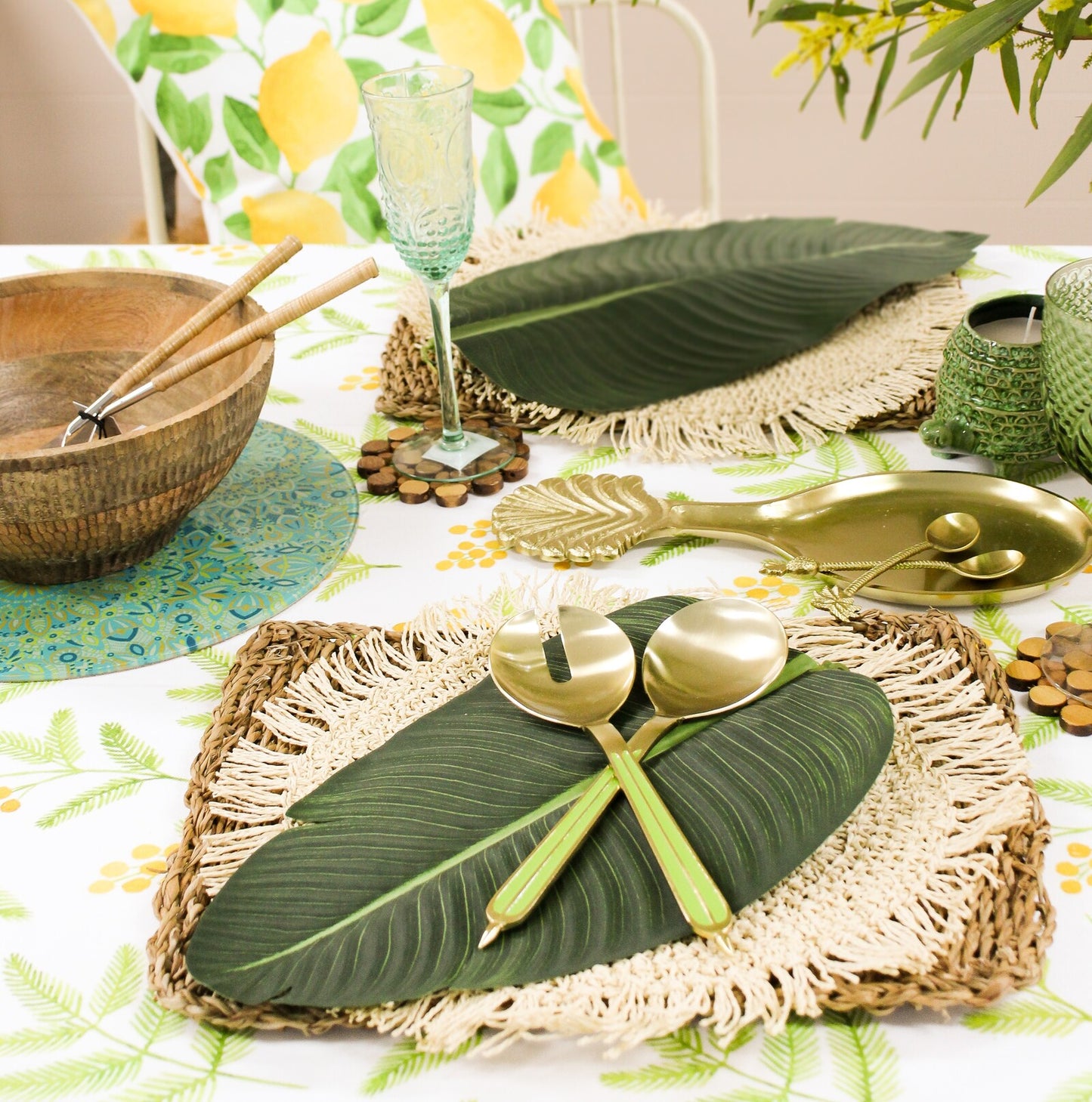 Decorative table setting with green leaves, gold cutlery, and a tropical-themed tablecloth.