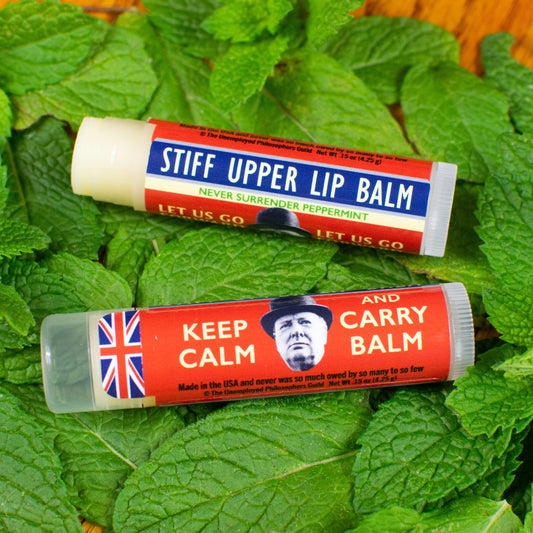 Two lip balms on a bed of green leaves, one labeled 'Stiff Upper Lip Balm' and the other 'Keep Calm and Carry Balm'.