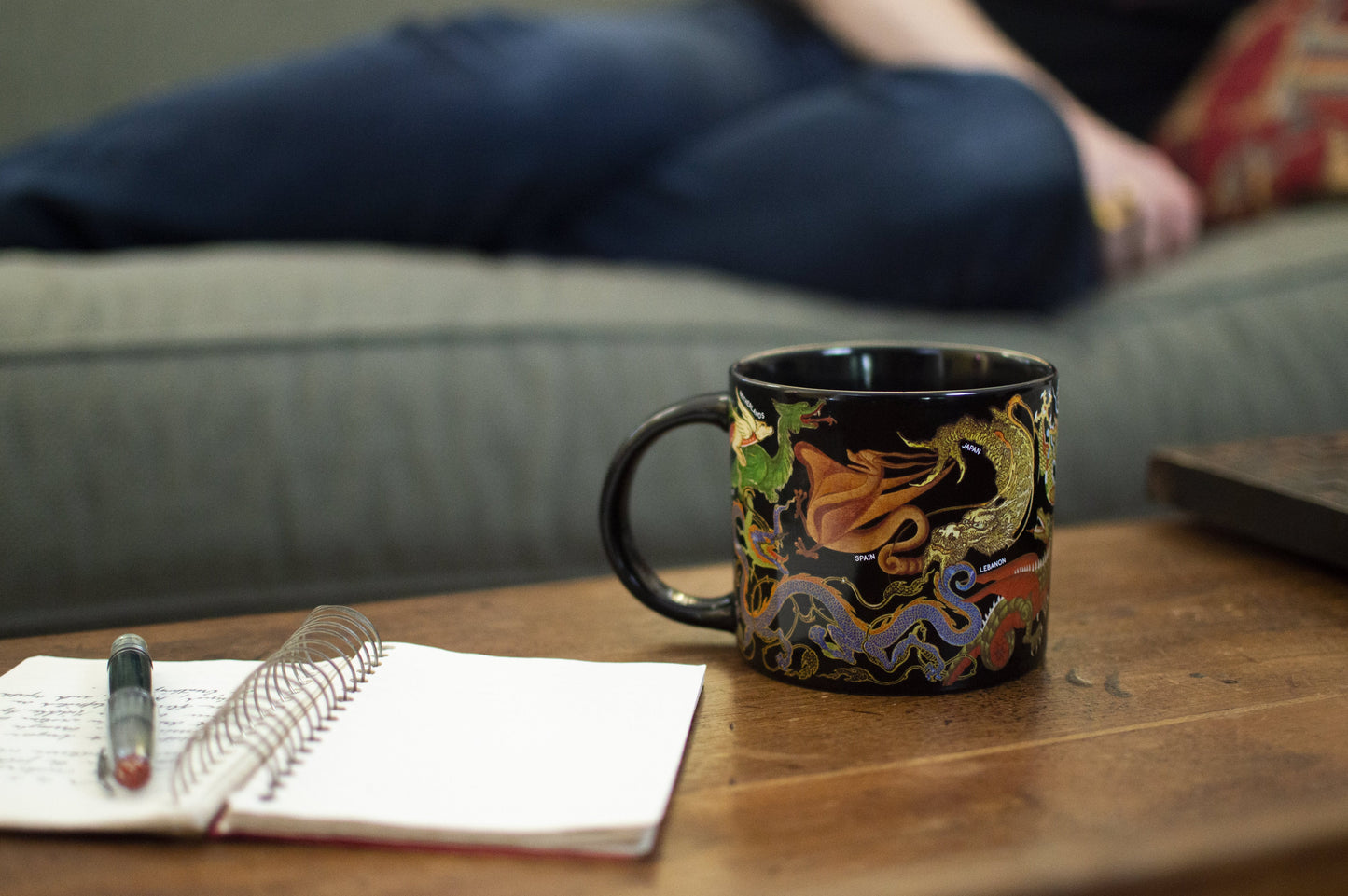 Decorative mug on a wooden table with a notebook and pen, blurred background