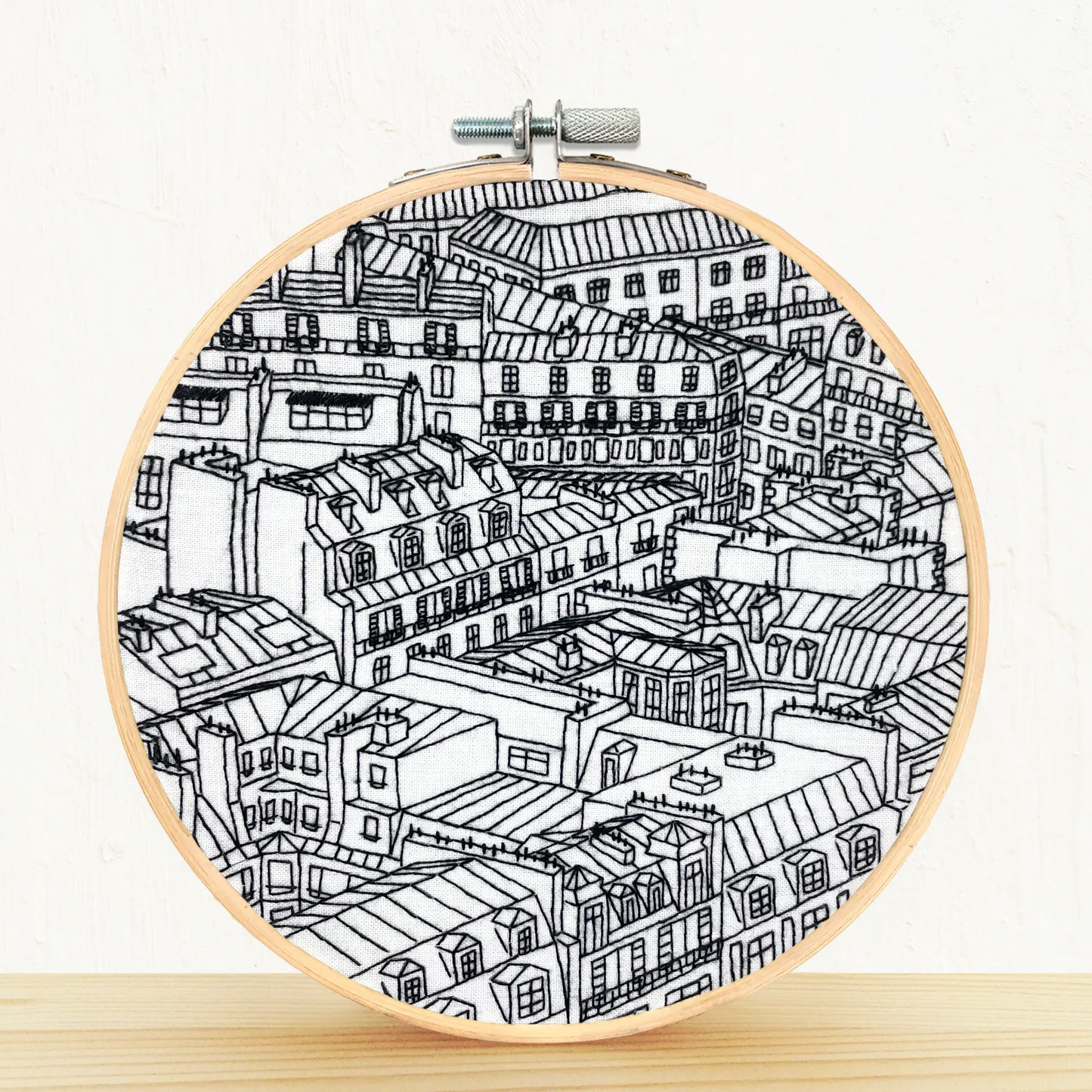 Completed embroidery loom placed on the pine shelf with whit background. The embroidery scene is of the Paris rooftops