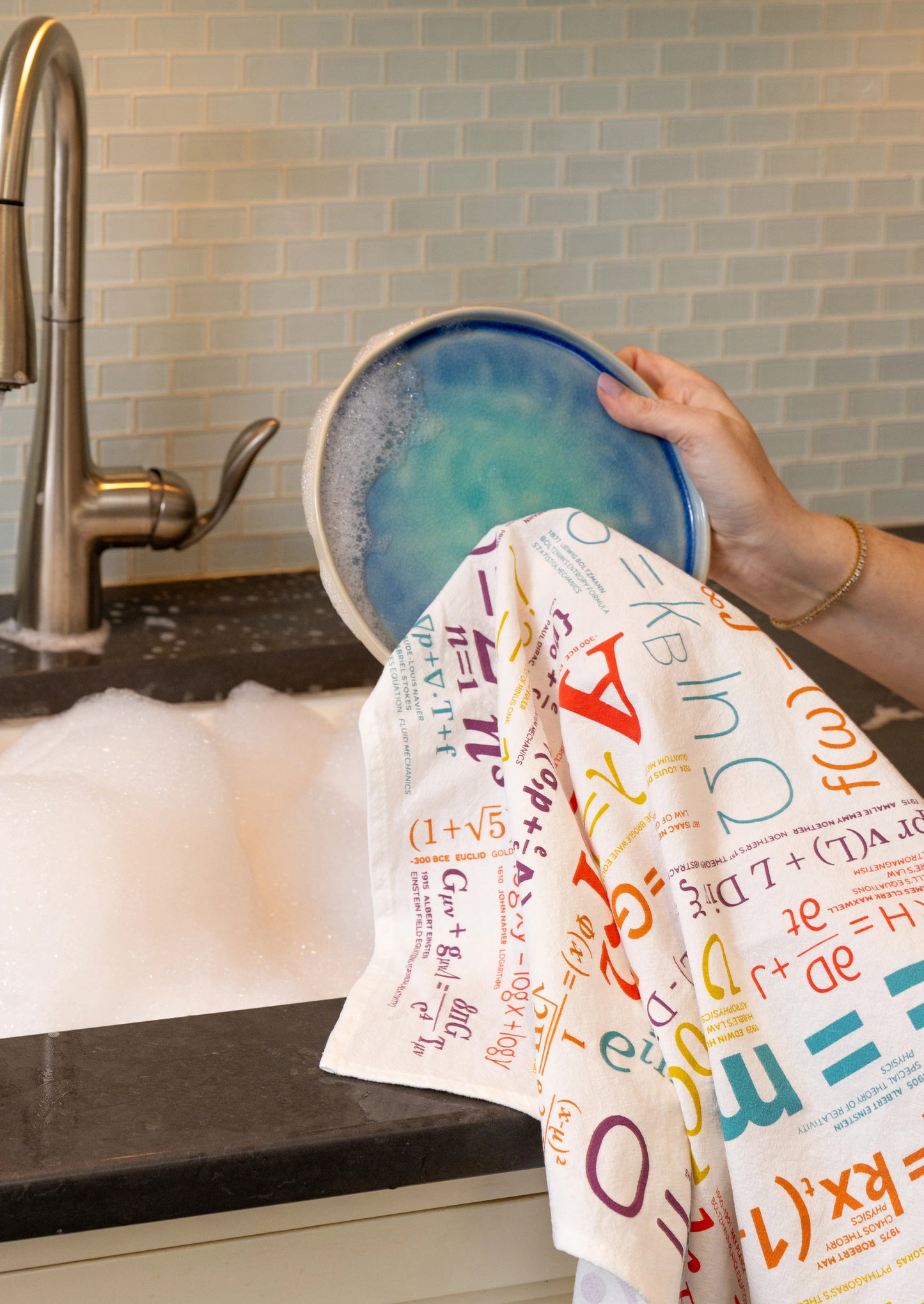 Person drying a dish with a colorful towel in a kitchen sink.