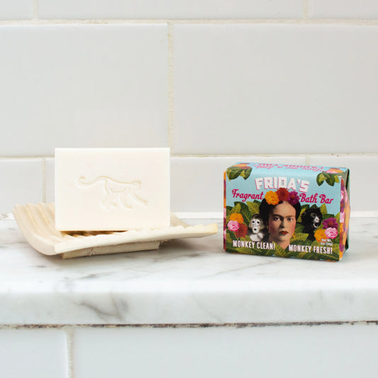 A bathroom setting with a bar of white soap and a packaged example of the Frida Kahlo hand soap.