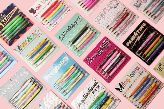 Colorful stationery items including pens sets in various cases on a pink background