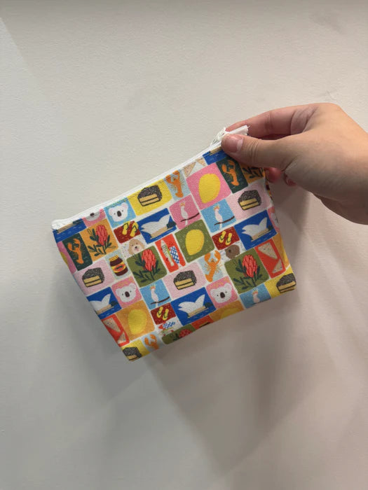 Suki McMaster Small travel pouch Aussie Icons with colorful pattern held by a hand on a light background