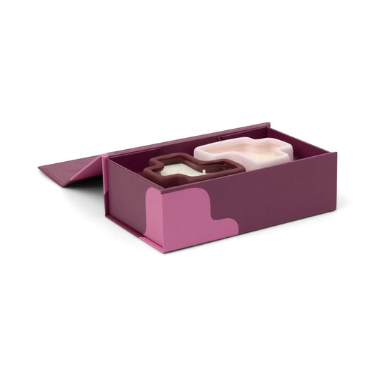 Pink and purple jigsaw shaped candles placed in a box on a white background
