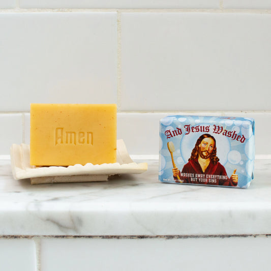 Bar of soap labeled 'Amen' on a soap dish with a packaging labeled 'And Jesus Washed' featuring an image of Jesus.