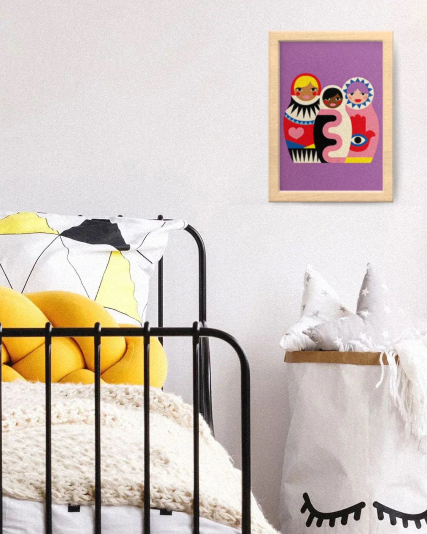 Framed artwork with colorful characters on a white wall above a black metal shelf with yellow cushions.