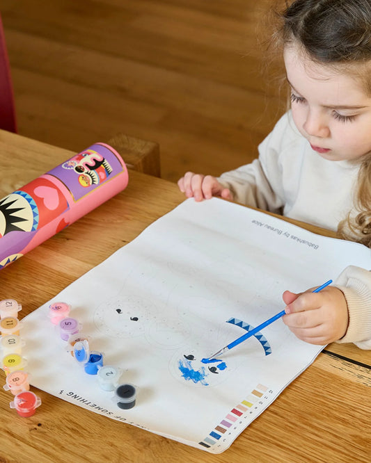 Child painting on a paper with a colorful water bottle in the background