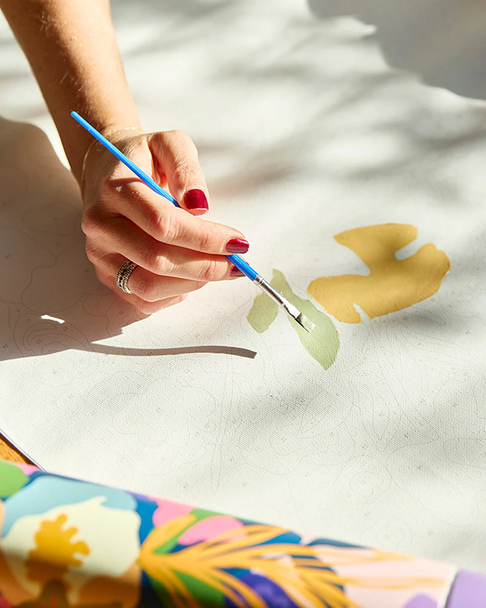 Person painting a yellow flower with a blue brush on a white surface.