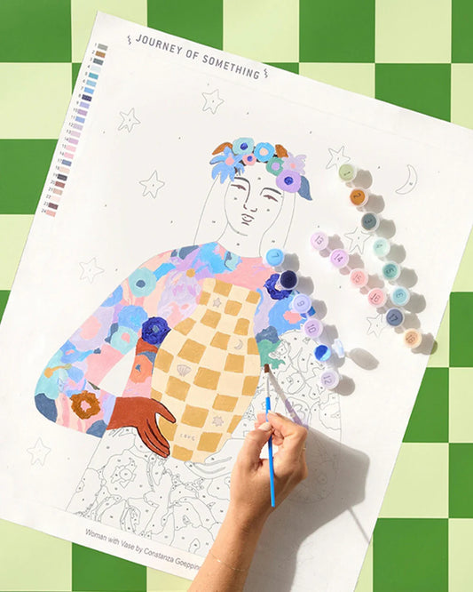 Paint by numbers process,Coloring art with a woman's face and floral elements on a green checkered tablecloth.
