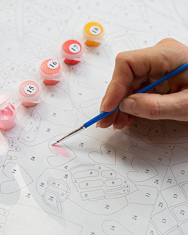 Hand painting a design on a piece of paper with small containers of paint and a brush.