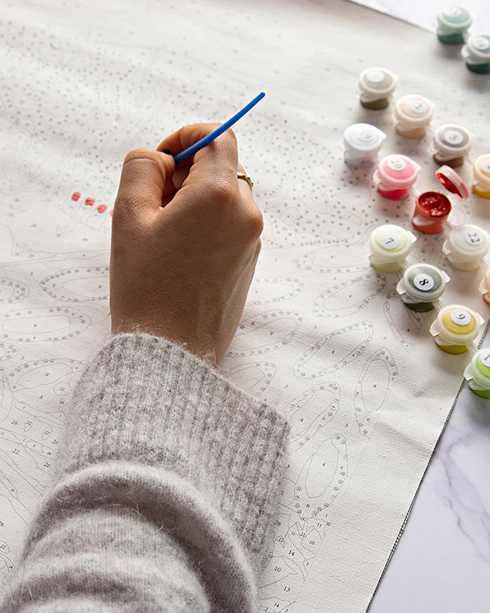 Person painting a small object with a brush on a textured surface, surrounded by paint containers.