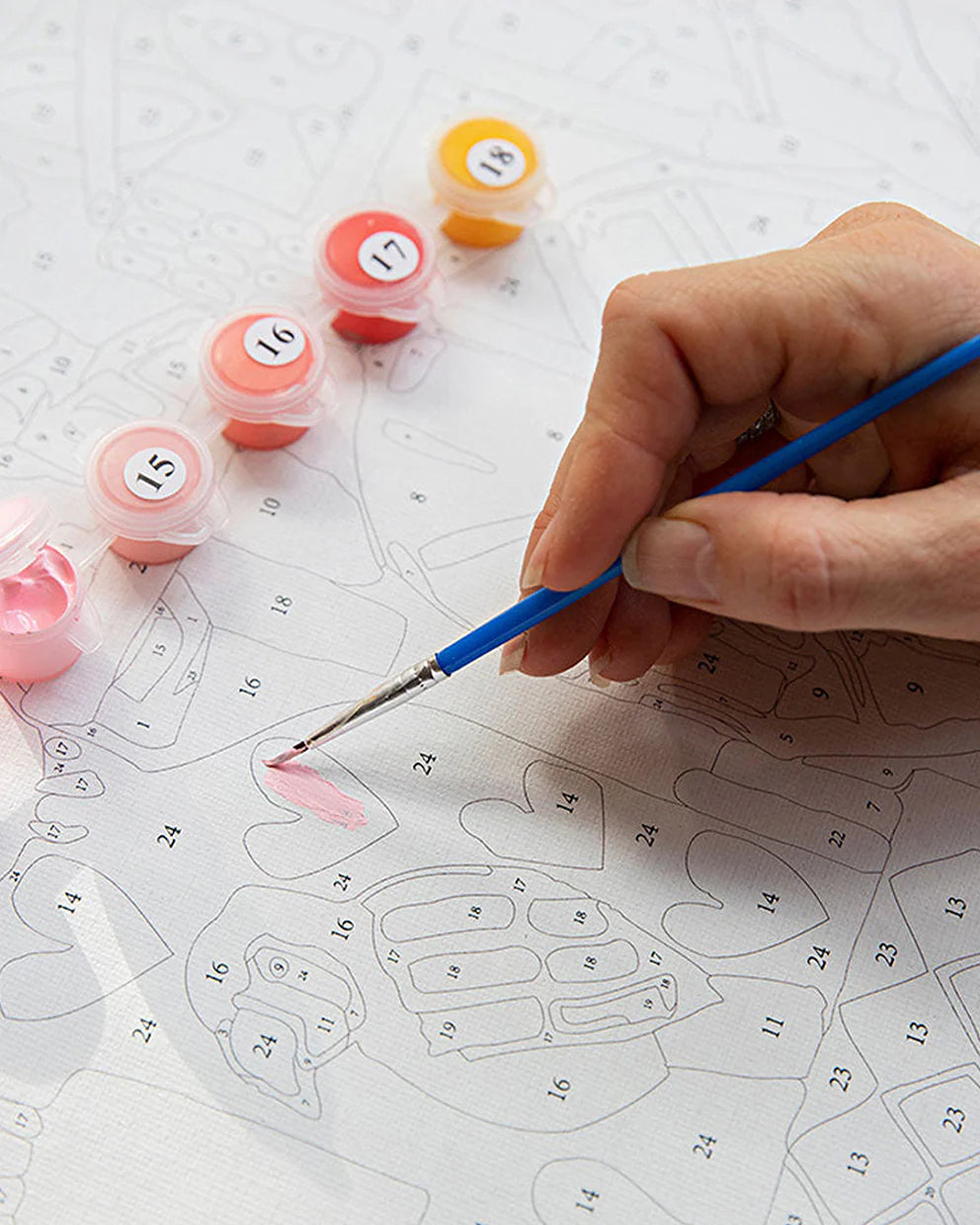 Person painting a pink design on a white surface with numbered templates