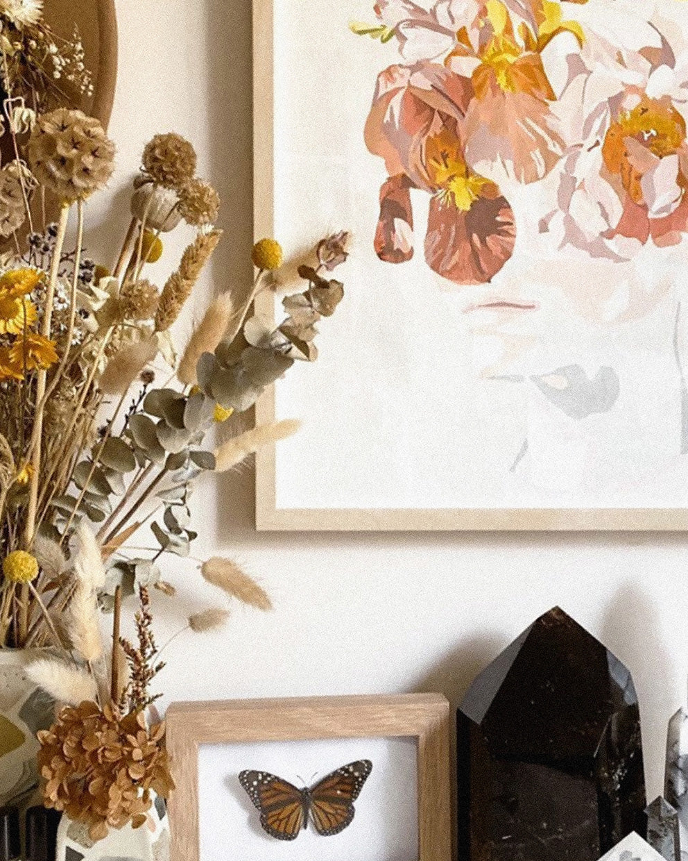Decorative wall with dried flowers, framed artwork, and crystals.