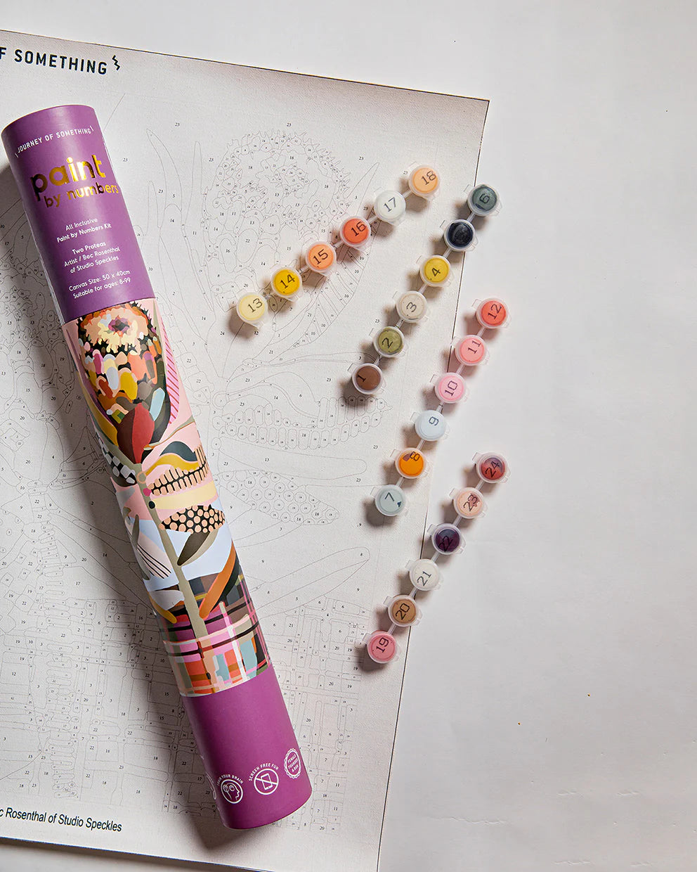 Colorful paint tubes arranged in a heart shape on a white surface with a branded tube next to them.
