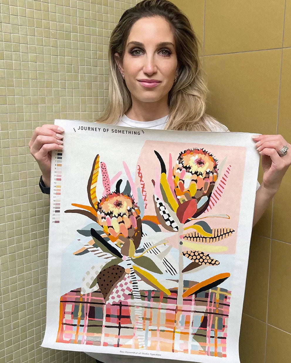 Woman holding a finished colorful "Two Proteas"abstract art print against a tiled wall.
