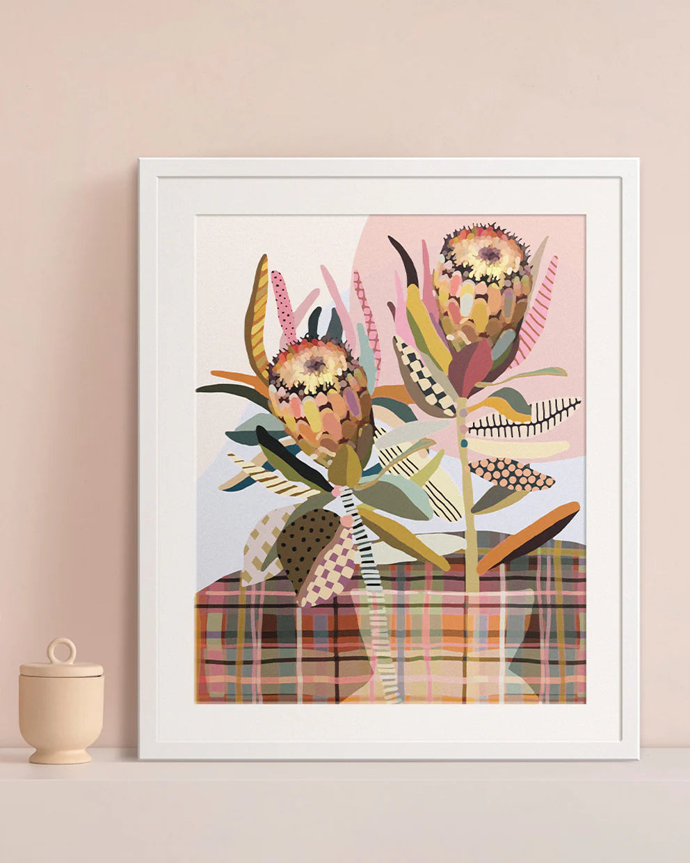 Framed artwork with abstract Protea floral design on a plaid background, displayed on a wall.