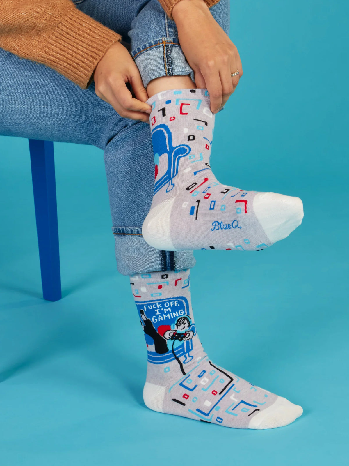A person pulling up one sock, whilst the resting leg has a slogan,"Fuck off I'm gaming. The background is blue.