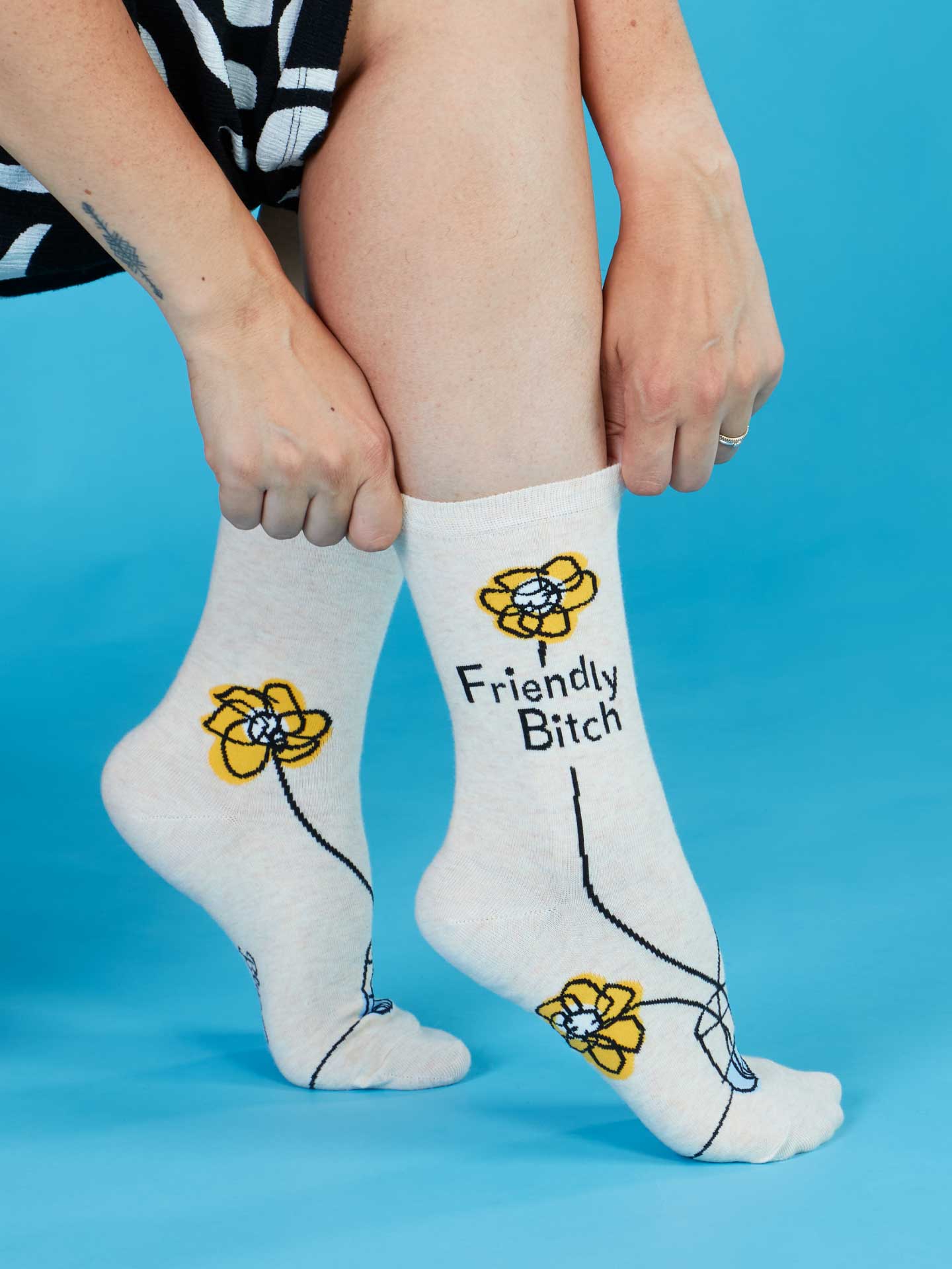 A lifestyle picture of a women's hands pulling up the friendly bitch socks. The background is blue.