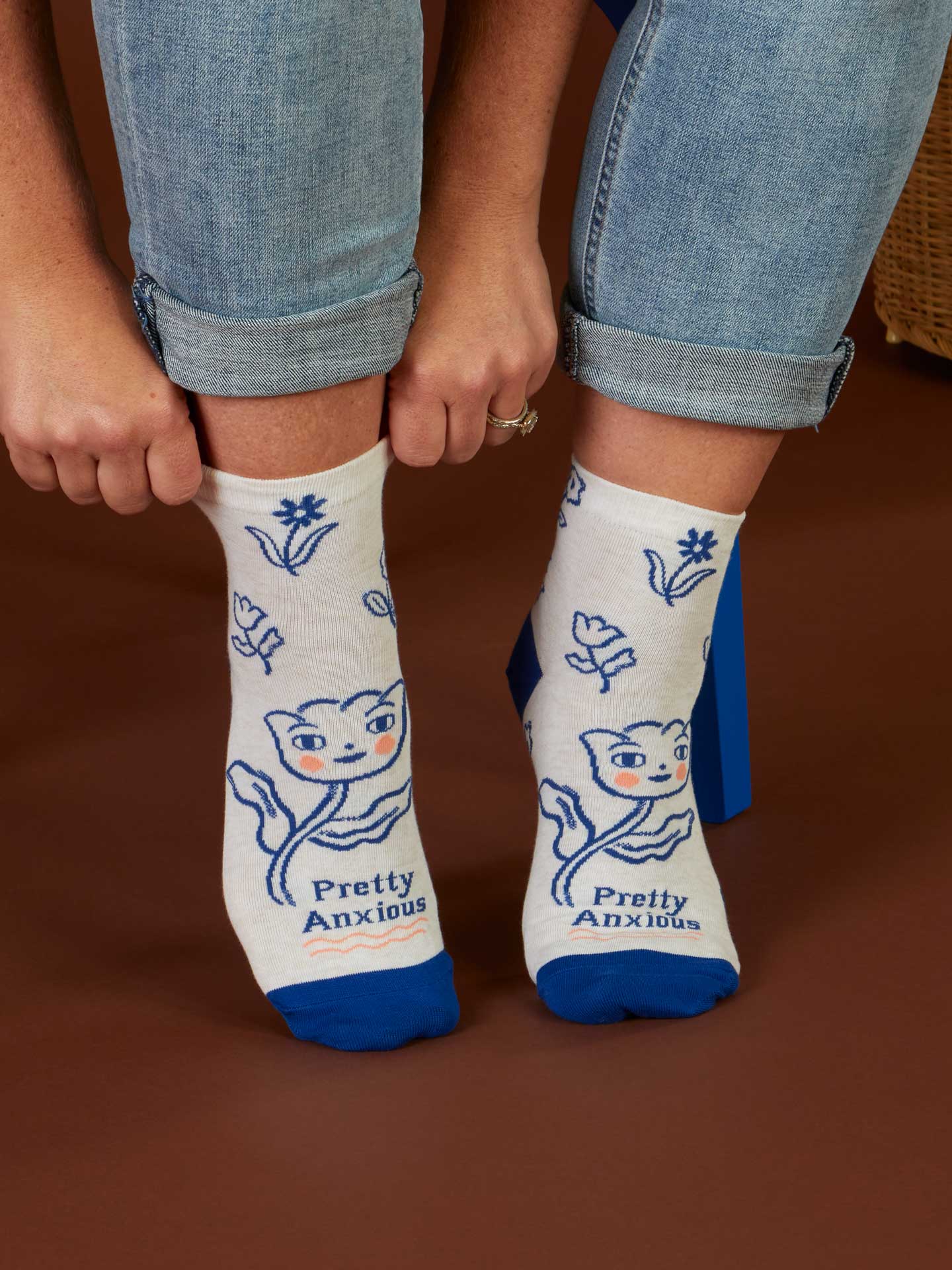 White socks with blue cat designs and 'Pretty Anxious' text worn by a person on a brown background