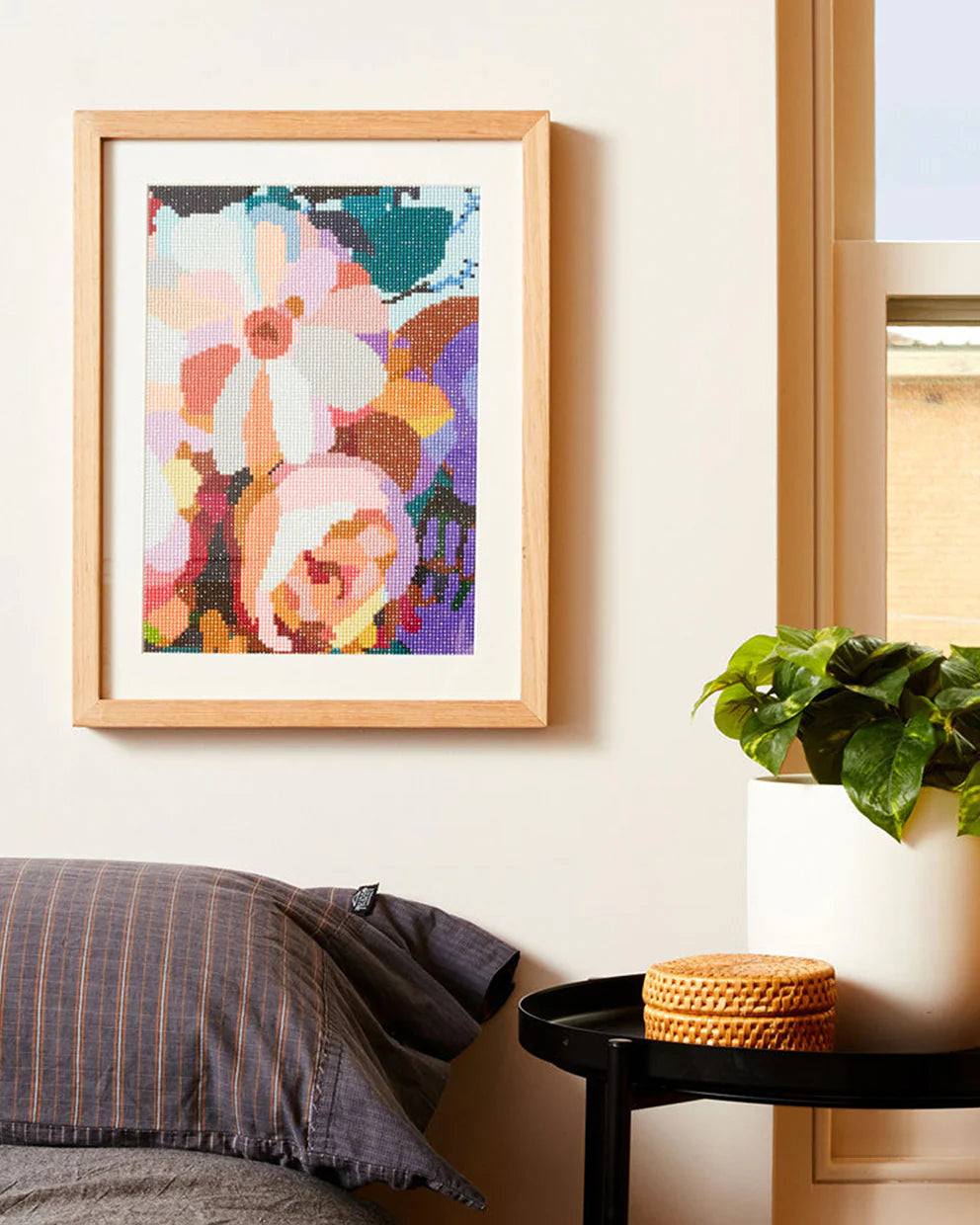 Framed floral artwork on a wall with a pillow and plant in the foreground