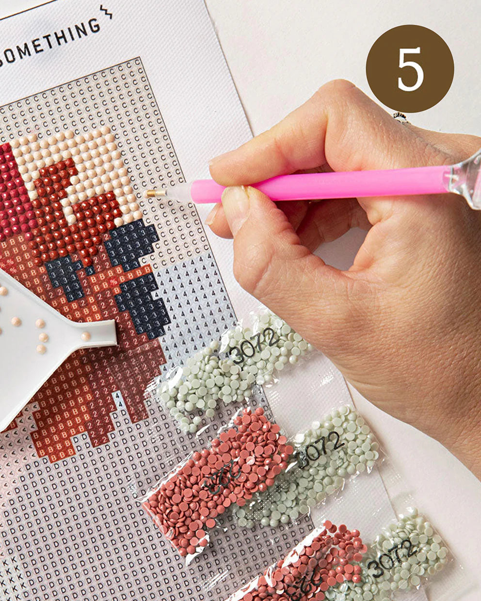 Person working on a sparkle art project with a pink needle and beads