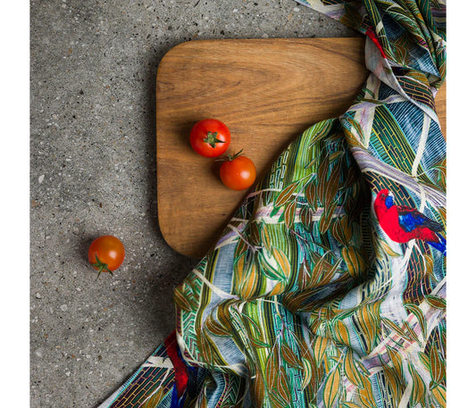 Wooden cutting board with tomatoes and a colorful fabric with Rosella bird pattern on a concrete surface