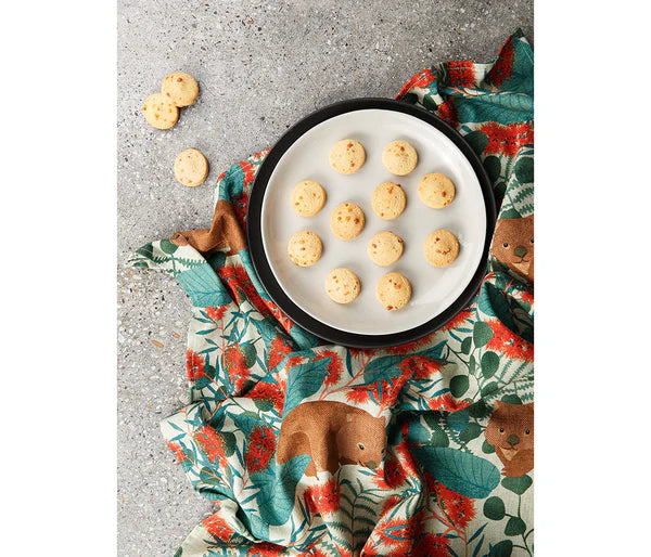 Tea towel featuring Australian wombat design- a plate of biscuits in the background