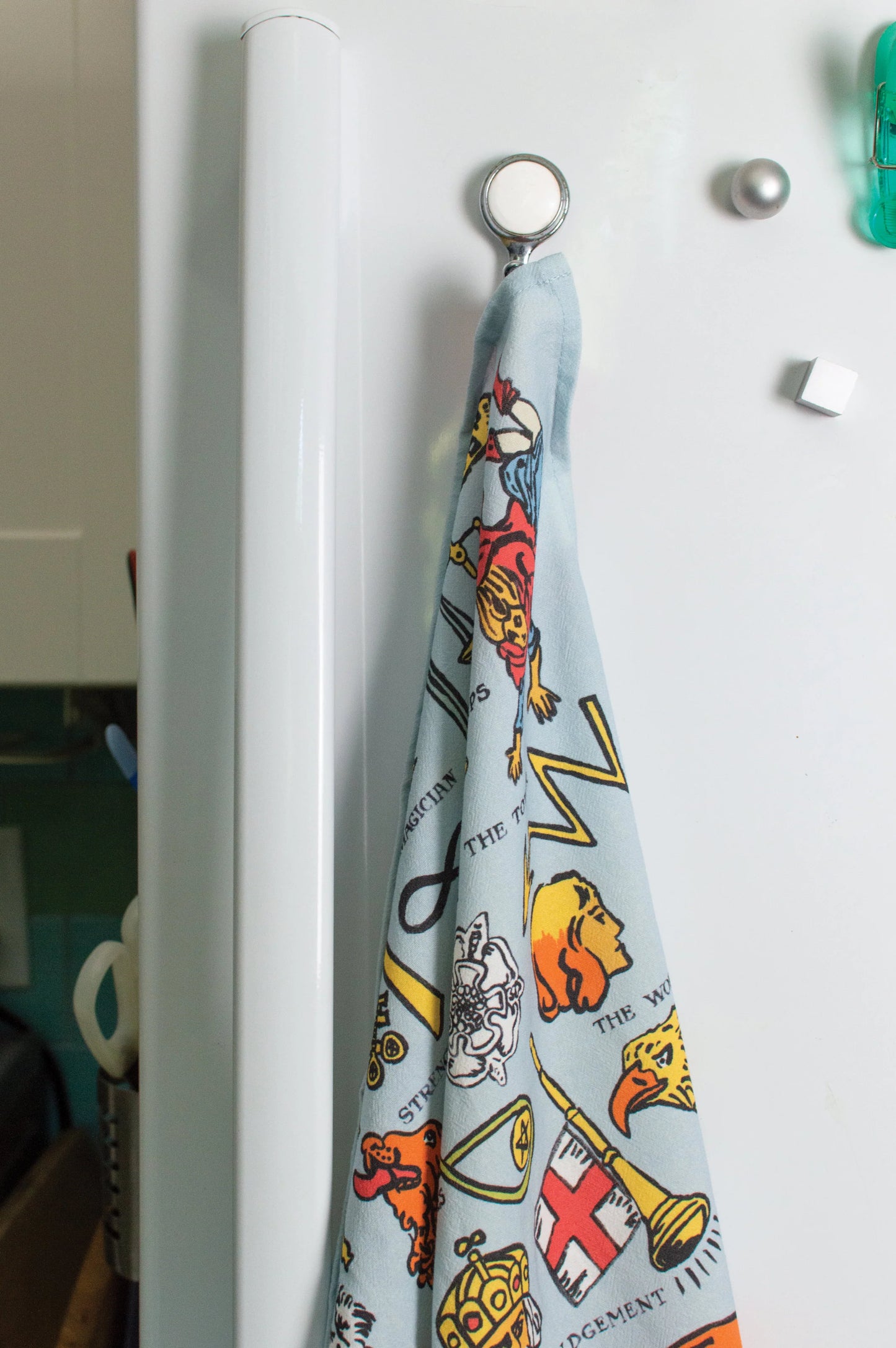 Colorful towel with tarot characters hanging on a white refrigerator.