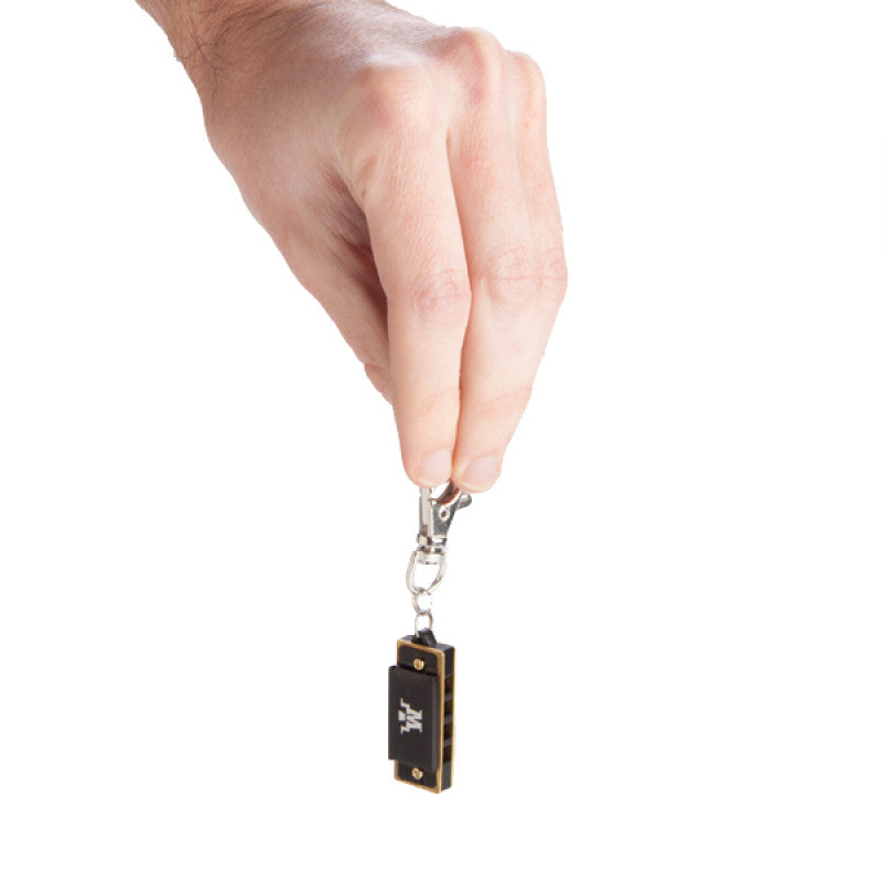 A hand holding a World's smallest harmonica with keyring on a white background