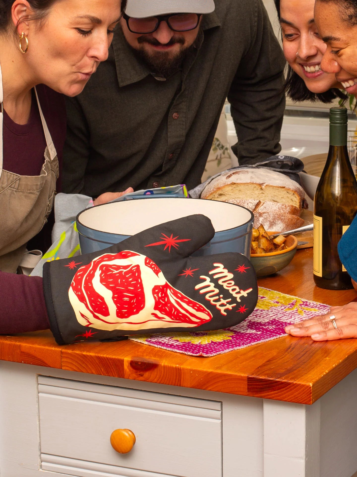 People in a kitchen with an oven mitt featuring a steak design on a wooden counter.