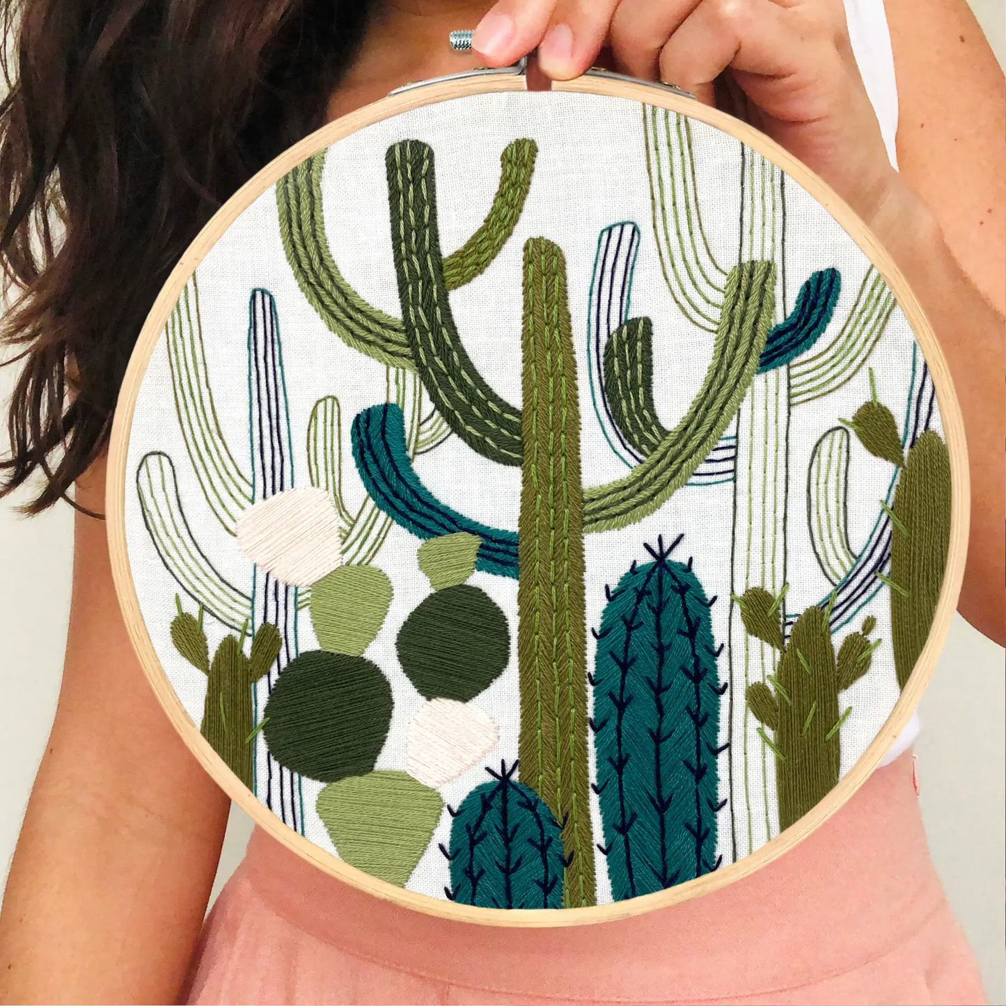 Women holding up the completed work of the embroidered cactus garden 6" hoop. Featuring an array of green needlepoint.