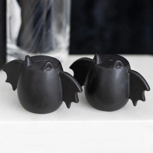 A set of two black bat winged salt and pepper shakers on a photographic background.