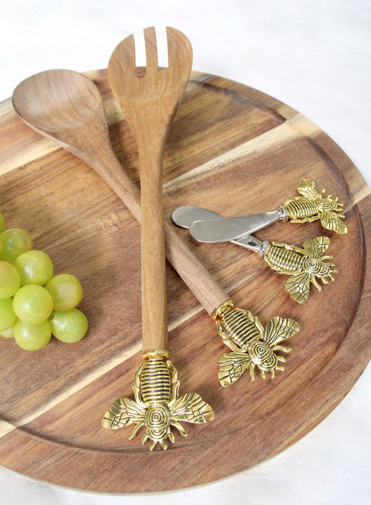 Wooden salad servers with bee handles on a wooden board with grapes.