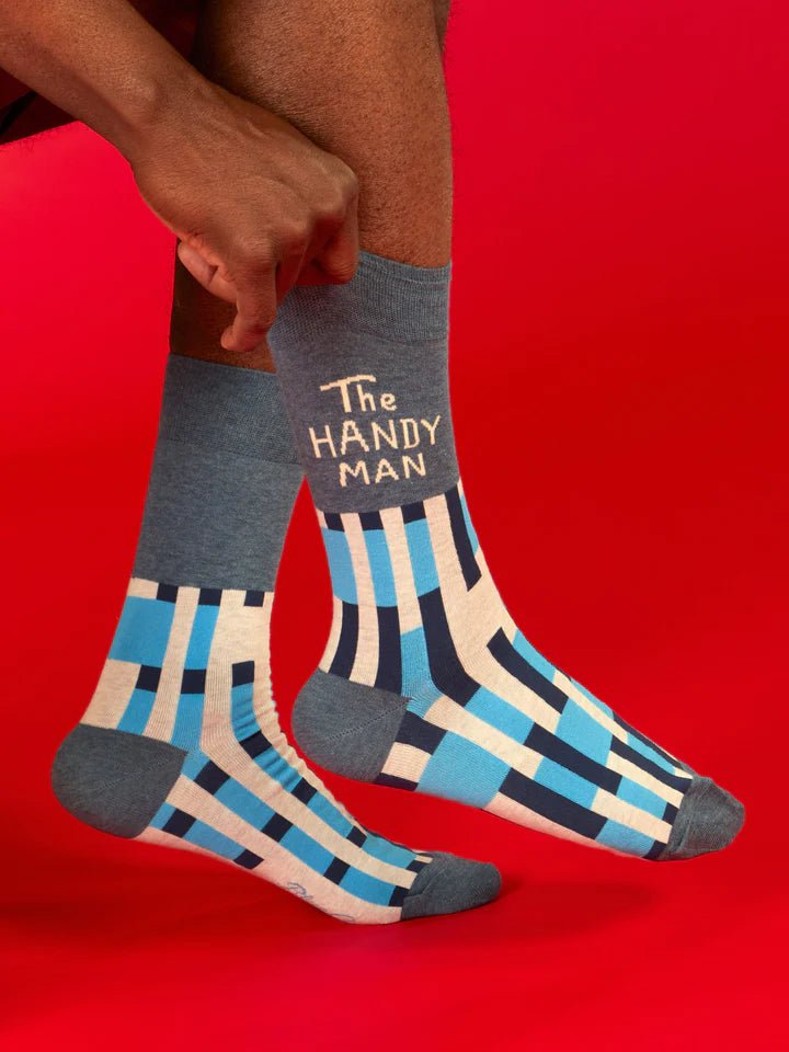 A man's hands pulling up a pair of BLUE Q Men's crew socks - The Handyman - on a red background |Gizmo Gifts