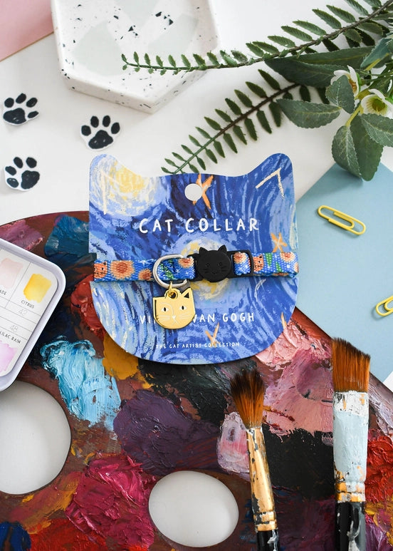 Cat collar with colorful design on a paint palette with art supplies and plants.