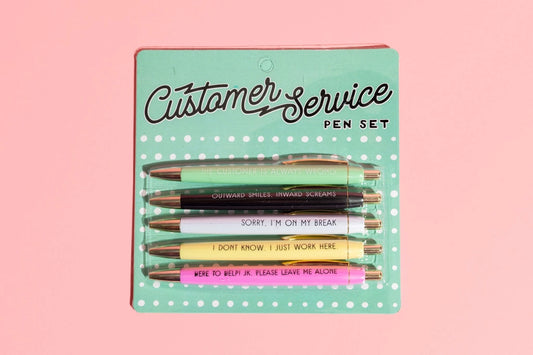 Set of pens with humorous sayings in packaging labeled 'Customer Service Pen Set' on a pink background