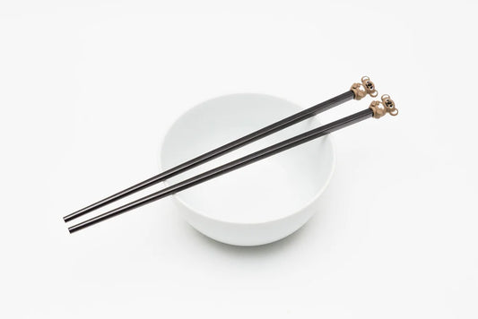 Black chopsticks with gold tips on a white bowl against a white background
