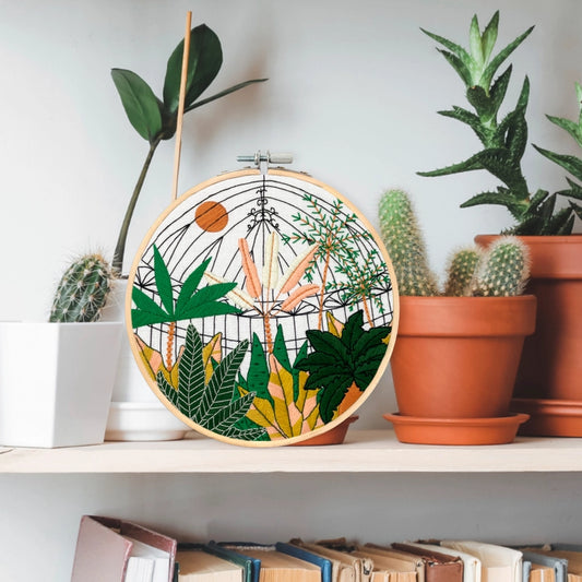 Lifestyle shot of the completed embroidery work - Botanical Greenhouse garden. It is sitting on a shelf between various planters.