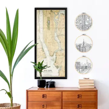 A lifestyle photo in a stylised setting. Three embroidery looms with complete scenes of New York city above a sideboard.