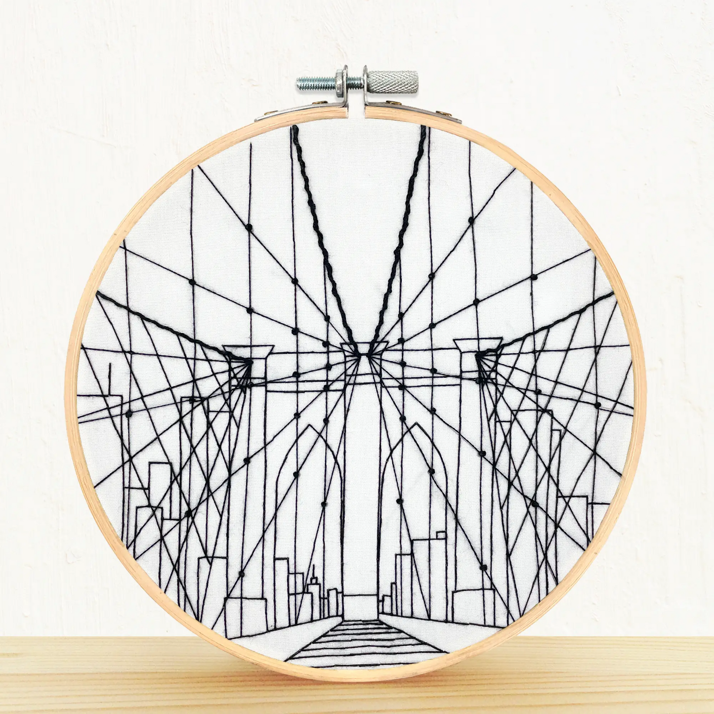Embroidery needlepoint Brooklyn Bridge/NYC sitting on a pine shelf with white background.