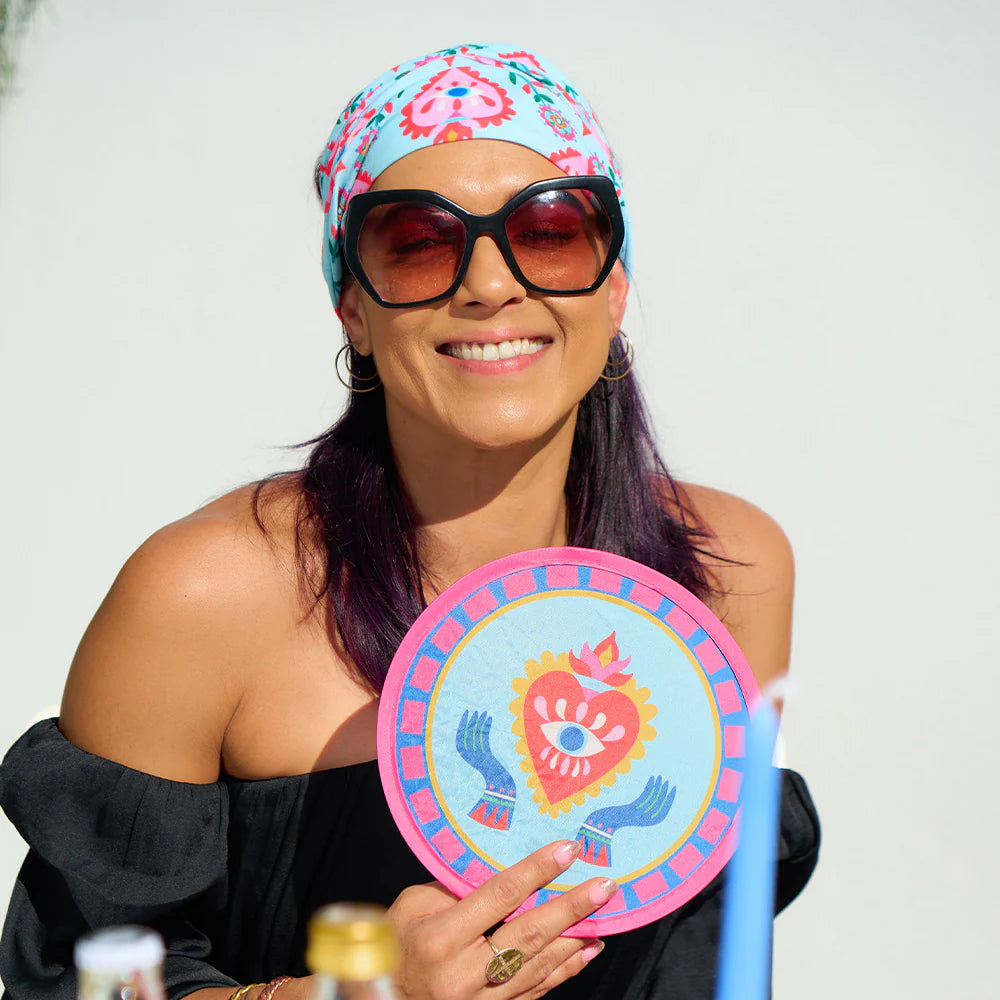 Woman wearing sunglasses and a headscarf, holding a colorful circular fan with a heart design.
