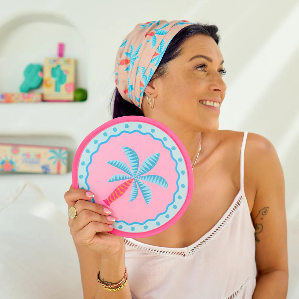 Woman holding a pink and blue decorative twist fan with a palm tree design.