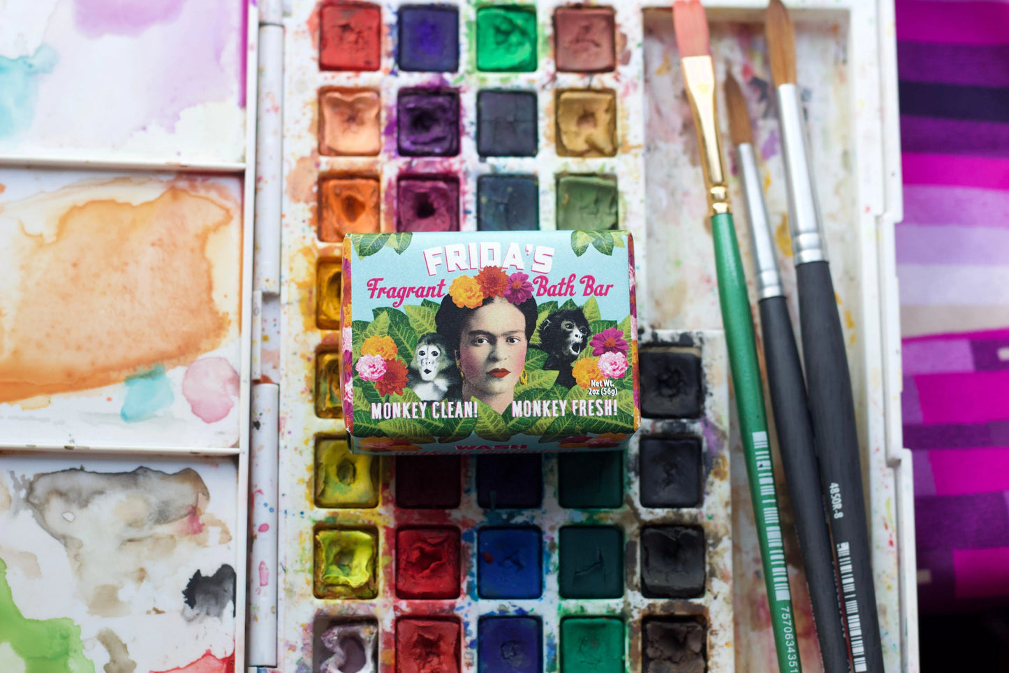 A paint palette with paint and brushes, a Frida Kahlo hand soap package in the centre.