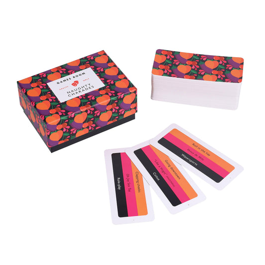GAMES ROOM - Naughty Charades open box with three cards in the foreground and a deck of cards in the upper right corner.