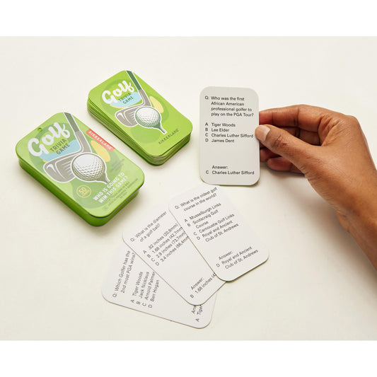 Hand holding a card from a golf-themed trivia game with green tin and cards on a white surface.