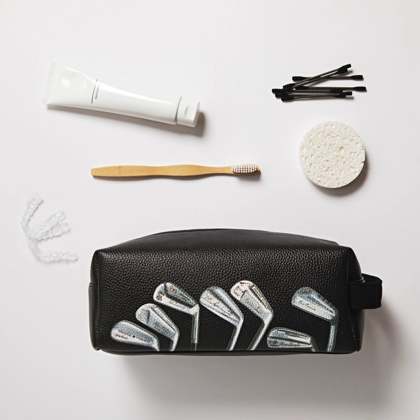 Black toiletry bag with golf club design, toothbrush, toothpaste, and sponges on a white background
